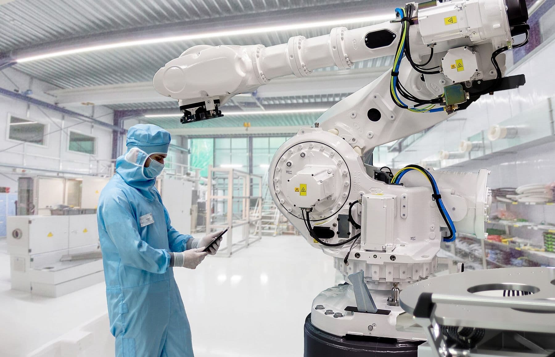 Engineer in cleanroom suit checking a large white six-axis industrial robot